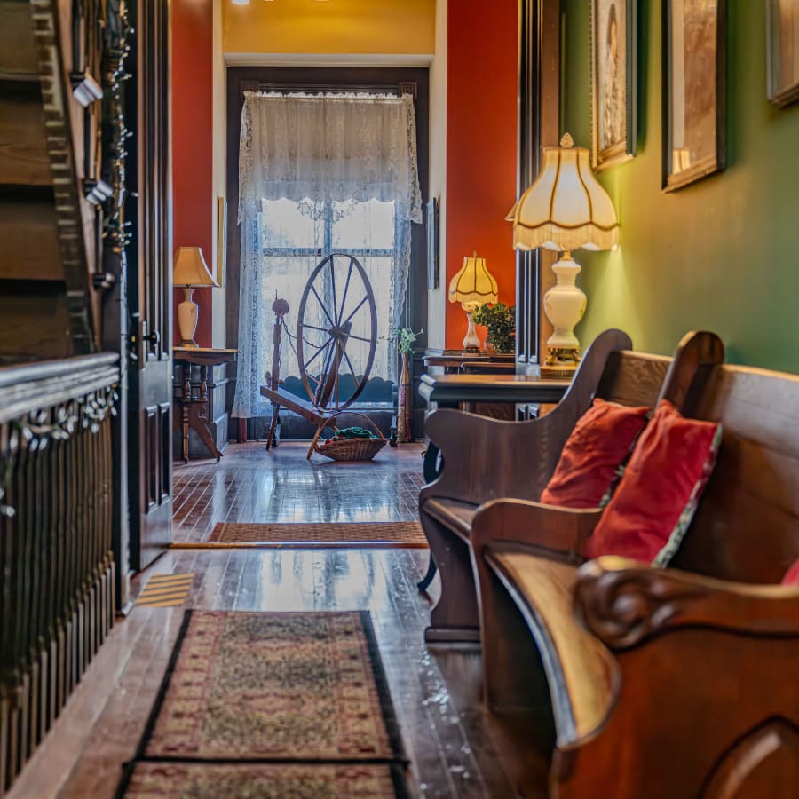 A warmly lit hallway with vintage furniture, a spinning wheel, and decorative lamps.