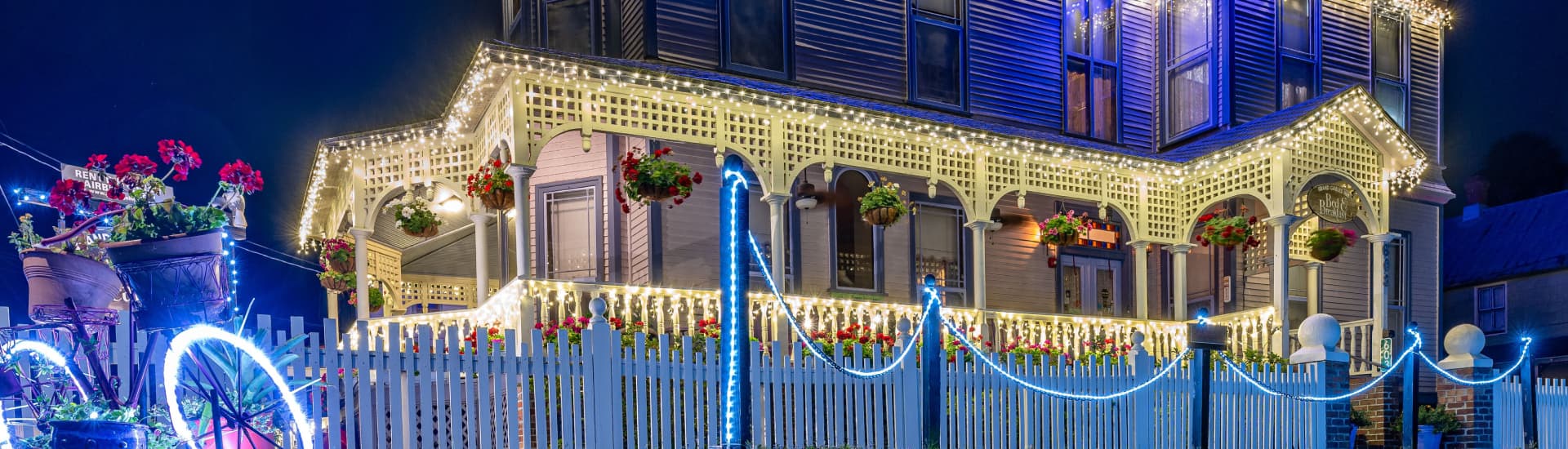 A beautifully decorated house with string lights and flower pots, set against a night sky.