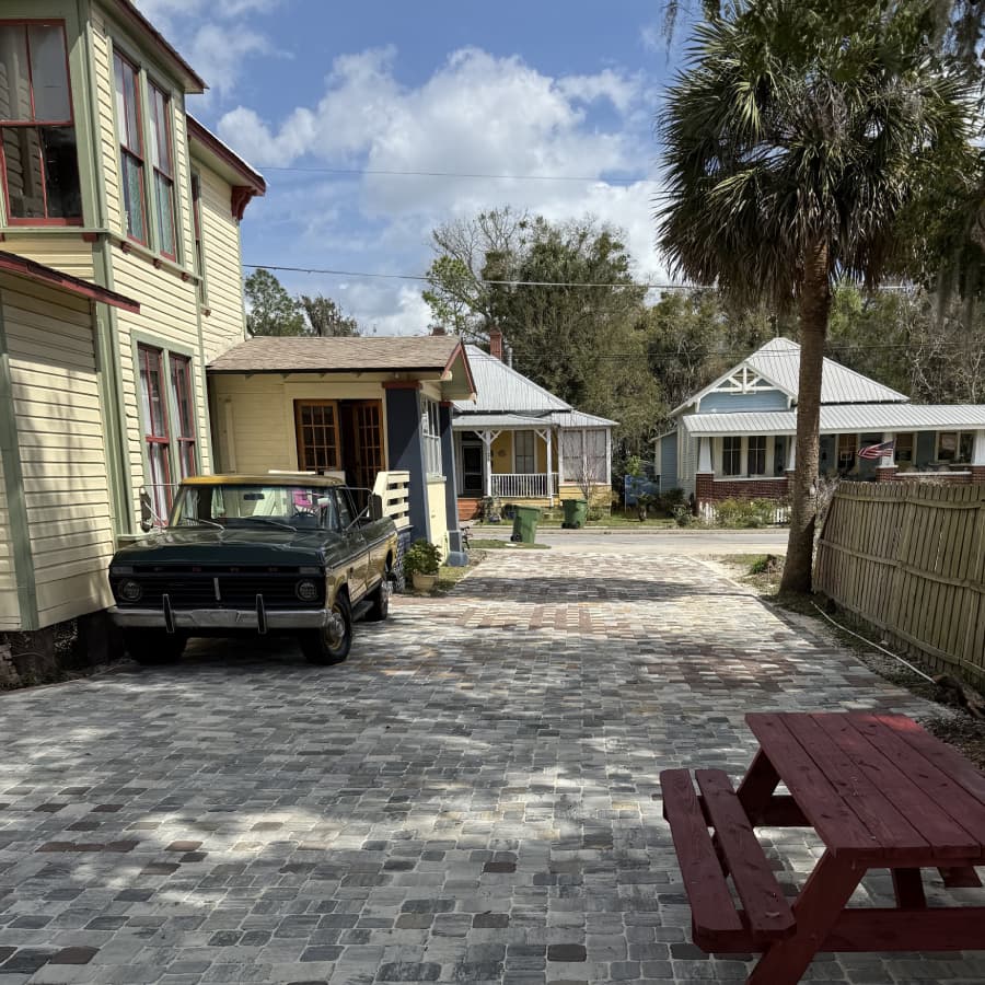 A narrow, brick-paved driveway surrounded by colorful houses and a vintage truck.