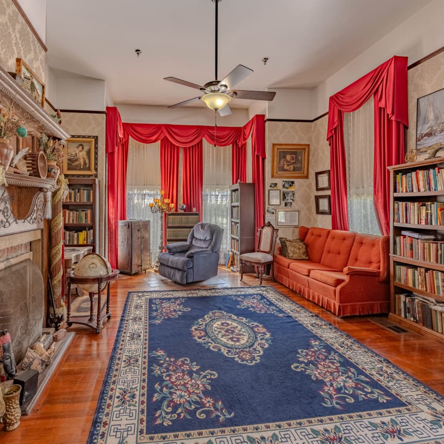 Cozy living room featuring a red accented window treatment, vintage furniture, and bookshelves.